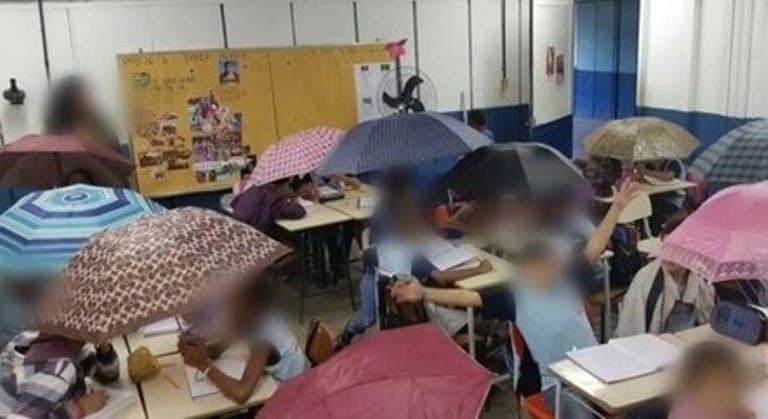 Alunos assistem aula com guarda-chuvas para se proteger de goteiras